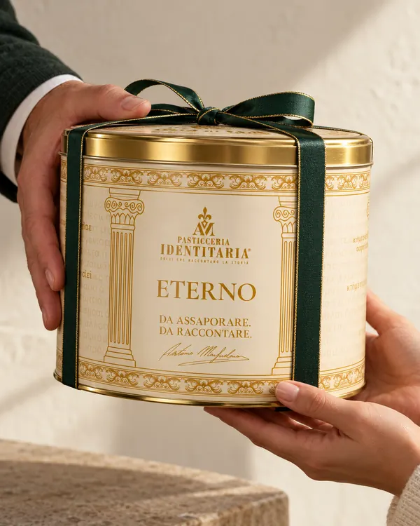 Mani che porgono in dono la latta avorio e oro dell’Eterno, chiusa da un nastro verde