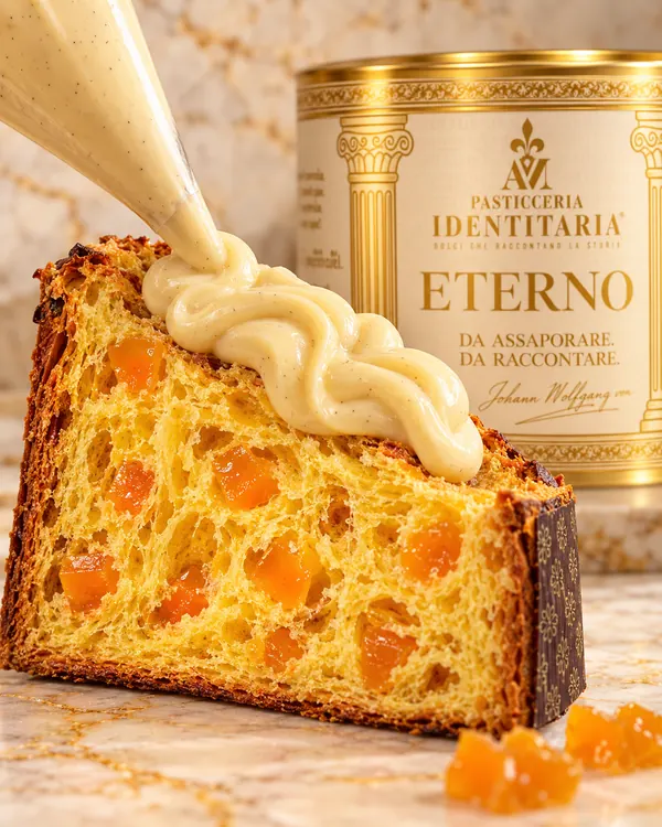 La crema di mandorla scende dalla sac à poche su una fetta di panettone Eterno, davanti alla latta avorio e oro